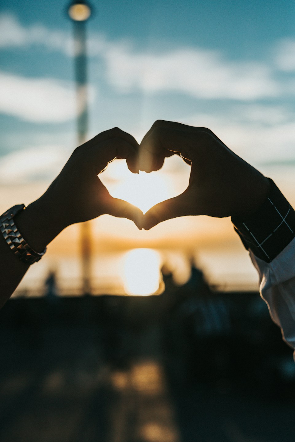 Hands forming a heart against a sunny sky